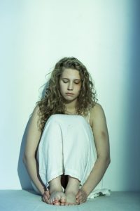 Young woman sitting on the floor with visible bruises, looking sad and distressed, symbolizing abuse, trauma, or domestic violence."
