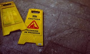 Yellow caution signs on tile floor indicating cleaning in progress and potential slip hazard.