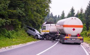 Tanker truck and passenger vehicle collision on rural road with forest background, representing serious truck accident or highway crash.