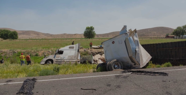 Overturned semi-truck and trailer off rural highway with workers on scene, representing serious commercial truck accident.