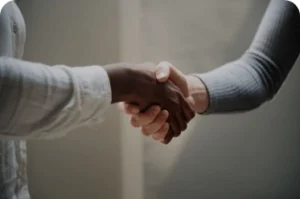 Close-up of two individuals shaking hands, one in a white shirt and the other in gray, symbolizing agreement, trust, and professional cooperation in a neutral indoor setting.