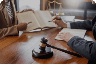 Two individuals seated at a wooden table reviewing legal documents, with a gavel and scales of justice present, symbolizing a formal legal consultation or case preparation.
