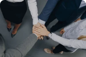 Top-down view of five professionals in business attire standing in a circle with hands stacked in the center, symbolizing unity, collaboration, and mutual support in a workplace setting.