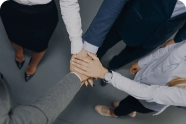 Top-down view of five professionals in business attire standing in a circle with hands stacked in the center, symbolizing unity, collaboration, and mutual support in a workplace setting.