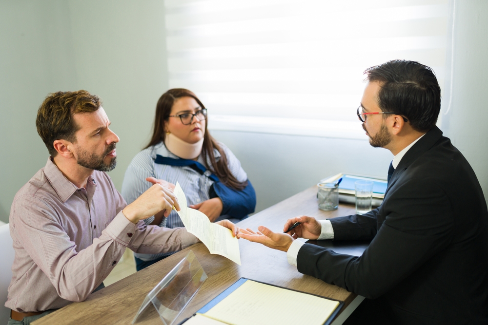 Couple meeting with a personal injury lawyer in an office, discussing paperwork and case details.