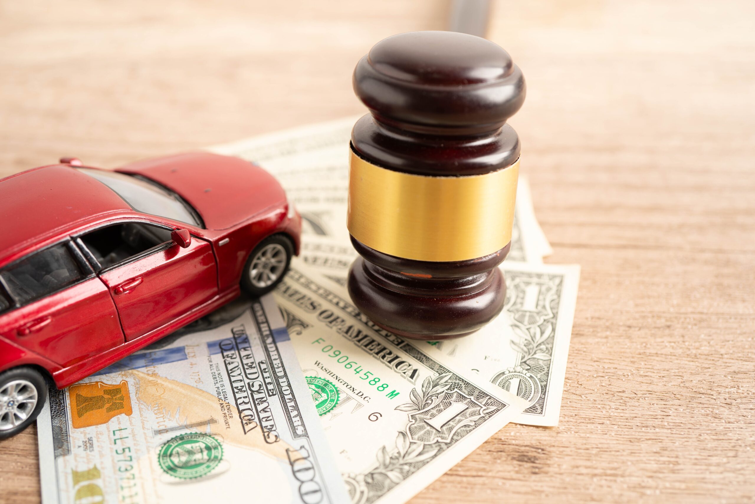 Judge gavel, money, and a red car representing a car accident claim and settlement