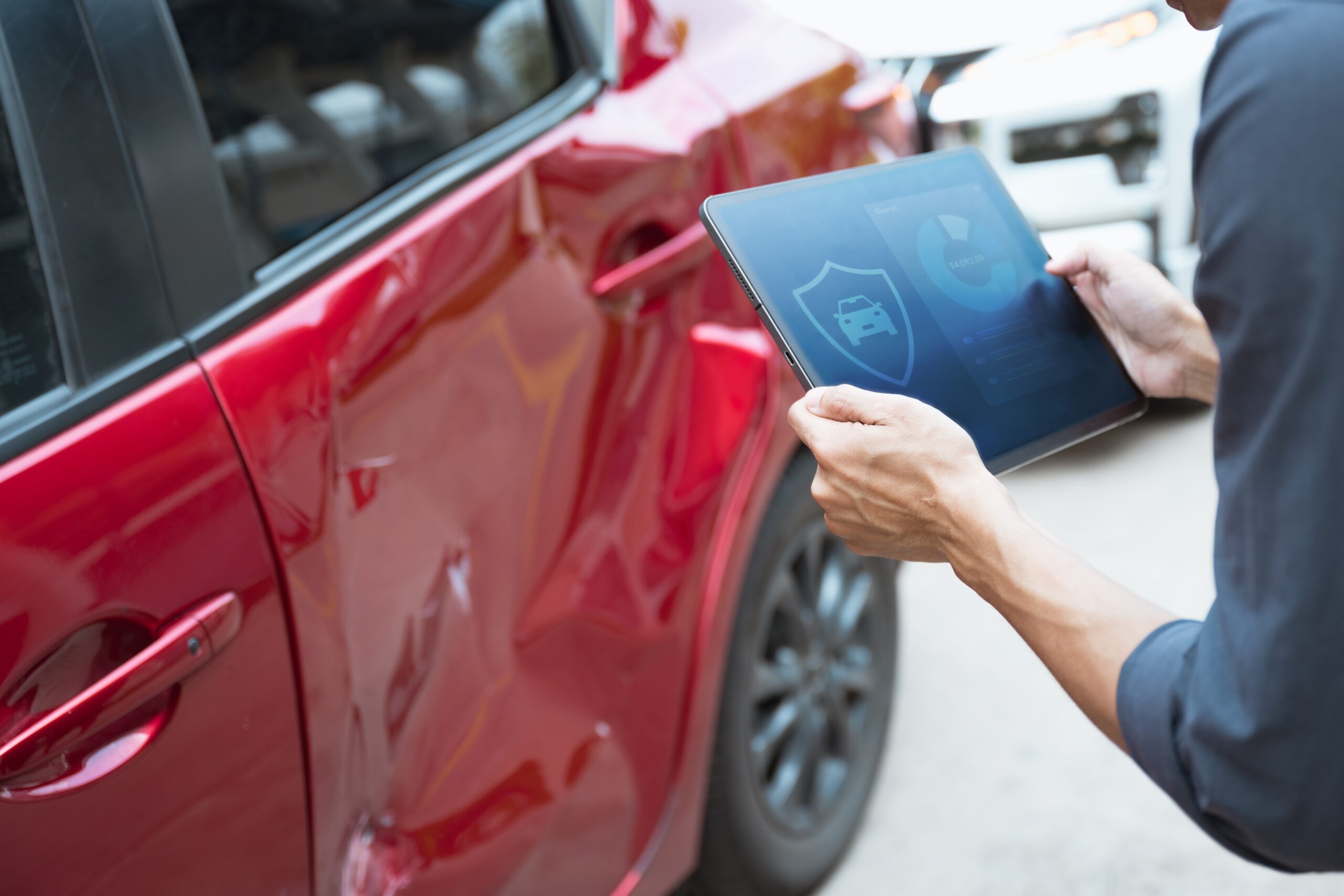 Person documenting car accident damage for an insurance claim using a tablet.